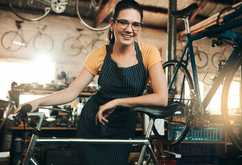 Woman, bicycle shop and portrait for maintenance job, startup with transport service. Bike, mechanic and female entrepreneur in workshop with glasses, happiness for sustainable business with apron