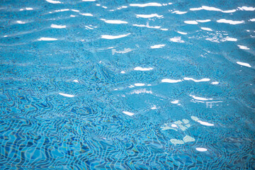 Close-up of blue tiled swimming pool water with sunlight reflections creating abstract patterns on the surface, evoking a refreshing and serene ambiance.