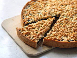A chocolate pie, cut, lies on a wooden board against a white table background. Homemade cakes, bakery, rustic cuisine, farm products