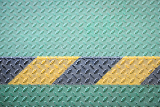 Green metal industrial floor with yellow and black hazard stripe.