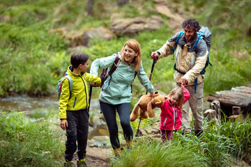 Happy family hiking by a stream with children carrying teddy bear