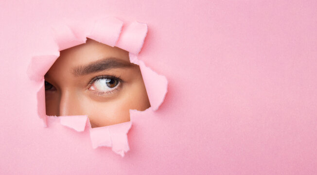 A lady with long brown hair is peeking out of a hole in pink paper. She is looking curious and excited, with her eyes wide open.
