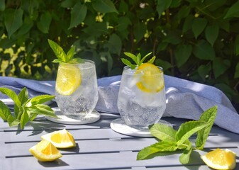 Summer refreshing drink with lemon slices on a table in the garden.