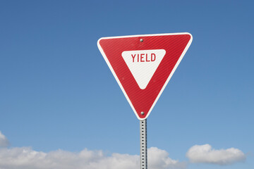 YIELD sign isolated against a blue sky background. A yield or give way sign indicates that merging...
