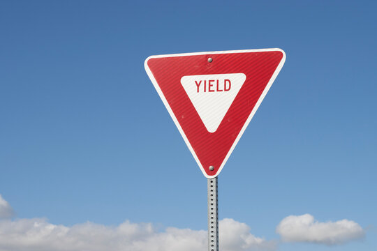 YIELD sign isolated against a blue sky background. A yield or give way sign indicates that merging drivers must prepare to stop if necessary to let a driver on another approach proceed.