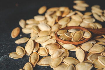Scattering pumpkin seeds in a wooden spoon on a black background