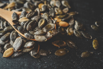 Scattering pumpkin seeds in a wooden spoon on a black background