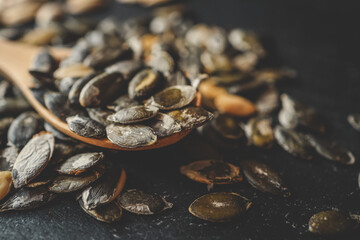 Scattering pumpkin seeds in a wooden spoon on a black background