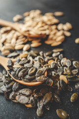 Scattering pumpkin seeds in a wooden spoon on a black background