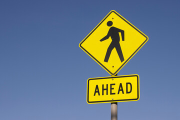 Pedestrian crossing ahead signage isolated against a clear blue sky background.