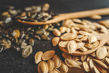 Scattering pumpkin seeds in a wooden spoon on a black background