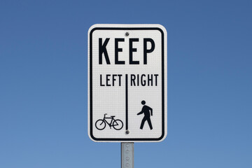 A sign informing cyclists and pedestrians of the division between the bike lane and the footpath, isolated against a blue sky background.