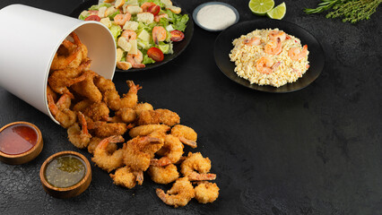 variety of seafood dishes. Fried shrimps, risotto and caesar salad with shrimp on black background with copy space. Starters and maim course