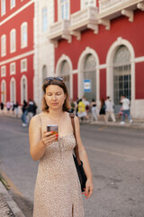 Fototapeta premium City travel concept. Tourist Woman looking at a ticket on her phone and waiting for transport at station, passenger books a ticket online through in the application. Copy space. Part of the series