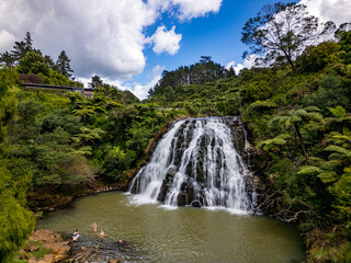 Drone View of waterfall surrounded by lush green forrest and bright blue sky. Owharoa Falls, Coromandel, New Zealand. 