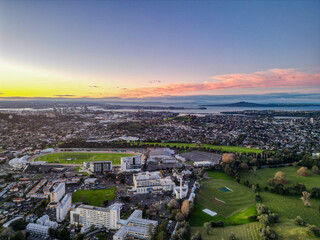 Auckland City Suburbs Skyline at Sunset. Hospital, sports fields and neighbourhoods meet pink and yellow horizon. 