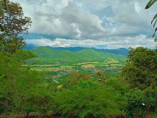 The panoramic landscape view of lush green mountain range covers with rain forest and cloudy rainy day in Chiang Mai, Thailand during rainy season. Small villages settles in the valley.