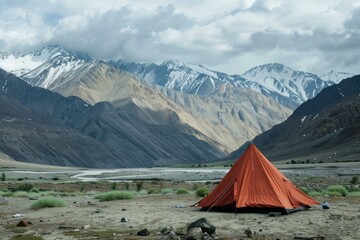 Experience the serene and tranquil mountain camping adventure amidst the stunning snowcapped alpine mountains with an orange tent