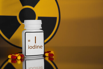 Bottle of medical iodine capsules and radiation sign on orange background. Space for text