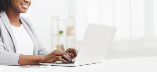 Cropped of professional black woman is typing on her laptop at work. The setting is sleek and organized, with bright lighting and a tidy workspace, emphasizing productivity, copy space, web-banner