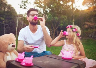 Dad, tea party and girl child in garden for nature picnic with toys, teddy bear and suitcase for table. Daughter, father and drink together for playing or entertainment, bonding and love in outdoor.