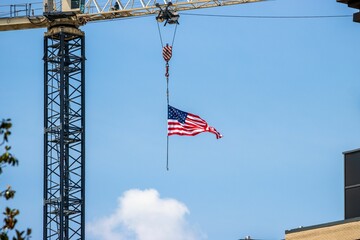American flag hanging from a construction crane against a clear blue sky.