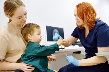 Baby and his mother are being seen by a pediatric neurologist in medical clinic. Doctor conducts tests, checks the reflexes, hearing of small patient using tuning fork. Highly qualified cure