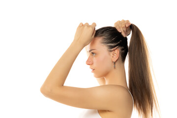 Fototapeta premium Side view of a young modern woman with a partially shaved head tying a ponytail on a white background