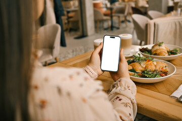 A phone with an isolated screen in hands against the background of breakfast in a cafe, an application for counting calories