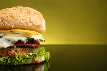 Delicious vegetarian burger on mirror surface against olive background, closeup. Space for text