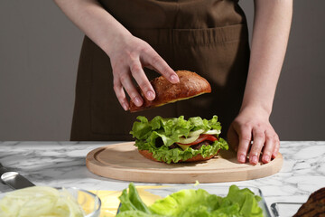 Woman making delicious vegetarian burger at white marble table, closeup