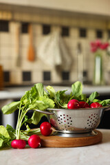 Metal colander with fresh radishes on white table