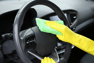 Woman cleaning steering wheel with rag in car, closeup