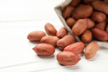 Obraz premium Fresh peanuts in sack on white wooden table, closeup