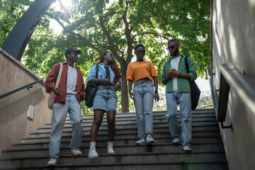 Stylish pleased group of african american students down to stairs to underpass chatting, gossips...