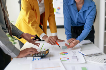 Team collaboration in a business meeting with professionals discussing charts and graphs on a desk in an office environment.