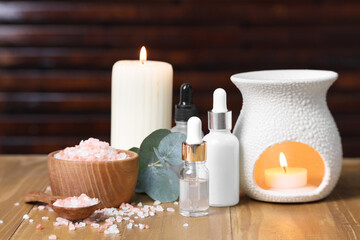 Different aromatherapy products, burning candles and eucalyptus leaves on wooden table