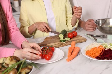 Friends cooking healthy vegetarian meal at white marble table in kitchen, closeup