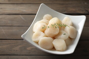 Fresh raw scallops and thyme in bowl on wooden table. Space for text