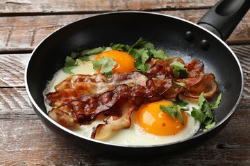 Tasty bacon, eggs and parsley in frying pan on wooden table, closeup