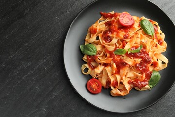 Delicious pasta with tomato sauce, vegetable and basil on dark textured table, top view. Space for text