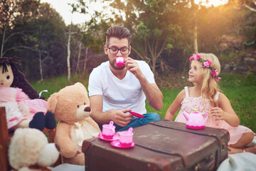 Father, tea party and girl child in garden for nature picnic with toys, teddy bear and suitcase for table. Daughter, dad and memory together for playing or entertainment, bonding and love in outdoor