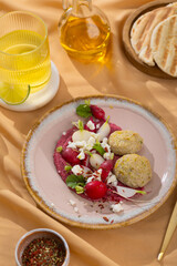 Healthy raw summer vegan snack plate. Flat-lay of beetroot humus dip with falafel and colorful fresh vegetables and greens on pink table background, top view. Clean eating, dieting, vegan