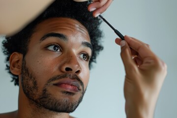diverse black guy applying makeup on his face, doing his eyebrows  - male skincare and  cosmetics copy space left	