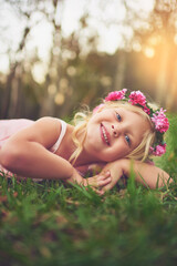 Girl, child and relax with portrait on lawn for fresh air in outdoor, playing and happiness with flower crown. Female kid, laying and field for carefree, enjoyment and summer childhood or fun youth.