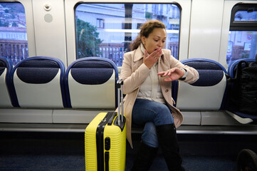Worried woman checking time on train with yellow suitcase, feeling stressed and anxious