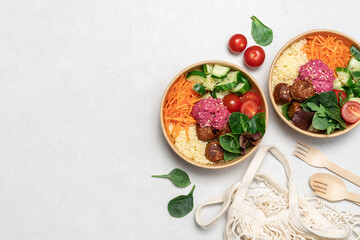 Healthy take away salad with vegan meatballs, vegetables, couscous and beetroot hummus  in disposable eco friendly paper containers on white background, top view