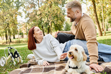 A couple and their dog relaxing on a blanket in a park.