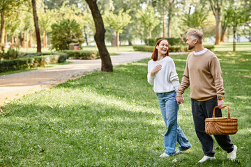 A couple leisurely walks through a park surrounded by lush greenery.