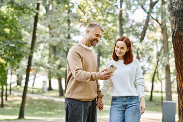 Couple standing in park, engrossed in cell phone.